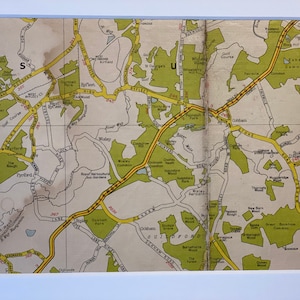 May include: A vintage map of the area around Guildford, Surrey, England. The map shows the location of various towns, villages, and landmarks, including Byfleet, Wisley, Ockham, and Cobham. The map is printed in black, brown, and yellow on a white background.