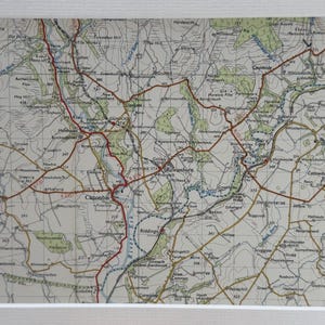 May include: A framed vintage map print showing a detailed topographical map with roads, rivers, and place names. The map has a cream background with brown, red, and green details. The print is set in a white mount.