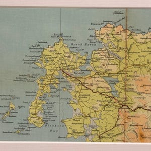 May include: A framed vintage map, featuring a detailed geographical representation in shades of yellow, green, and brown. The map includes a network of roads and place names, set against a light blue background. It is framed in a white border.