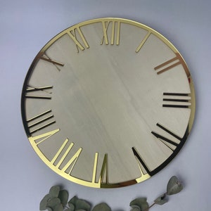 May include: A gold-colored clock face with Roman numerals. The clock face is round and has a white background.