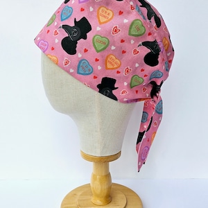 May include: Pink surgical scrub hat with a black and white print of a plague doctor and candy hearts with phrases like "RIP", "URA GONER", "SOON", "C U IN HELL", "DROP DEAD", "LETS GO VIRAL", and "DIE".