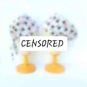 Könnte beinhalten: Zwei dekorative Eierbecher mit floralem Muster. Die Halter sind gelb mit weißem Sockel und einem floralen Muster in Rosa und Schwarz. Das Wort "CENSORED" steht auf dem Bild.