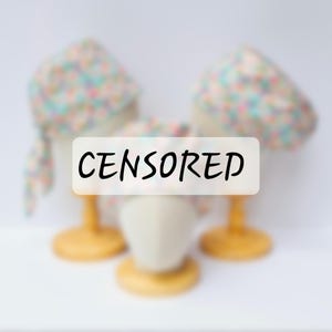 May include: Three fabric head coverings with a floral pattern in pastel colours, displayed on mannequin heads with wooden stands. The word "CENSORED" is written across the image in black text.