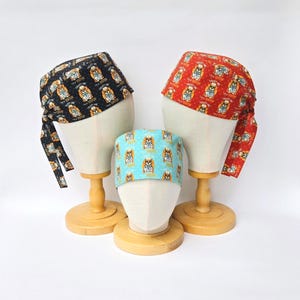 以下が含まれることがあります： マネキンの頭に3つの模様入りのスクラブキャップ。1つは、犬の医者のグラフィックと「I'M A DOCTOR, TRUST ME」のテキストが繰り返される黒色です。もう1つは、同じグラフィックとテキストの赤色です。3つ目は、同じ犬の医者のグラフィックのライトブルーです。