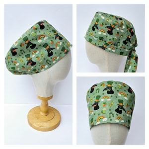 以下が含まれることがあります： 緑色の手術用スクラブハットに、黒と緑のレプリコーン、虹、クローバーのプリントが施されています。