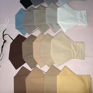 May include: A collection of 18 fabric face masks in various shades of brown, beige, and blue. The masks are arranged in rows, with the darkest shades at the bottom and the lightest shades at the top.