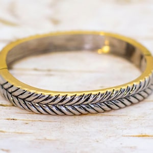 Puede incluir: Un brazalete de oro y plata con un diseño trenzado.