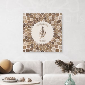 Puede incluir: Una impresi&oacute;n de arte de caligraf&iacute;a isl&aacute;mica beige y marr&oacute;n con la palabra "Allah" en el centro, rodeada de un patr&oacute;n geom&eacute;trico de hojas. La impresi&oacute;n est&aacute; colgada en una pared blanca sobre un sof&aacute; blanco con almohadas marrones y una mesa de caf&eacute; de madera.