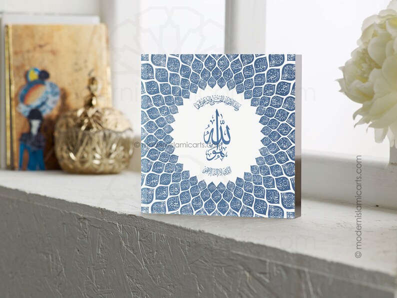 May include: A square, white canvas print with a blue and white design. The design features a circle with the Arabic word "Allah" in the center, surrounded by a pattern of blue leaves. The leaves are arranged in a circular pattern around the circle.