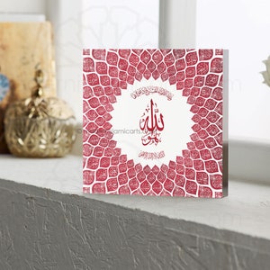 May include: A red and white square wall art piece with an intricate design of Arabic calligraphy. The design features a circular frame with the word "Allah" in the center, surrounded by a pattern of leaves.