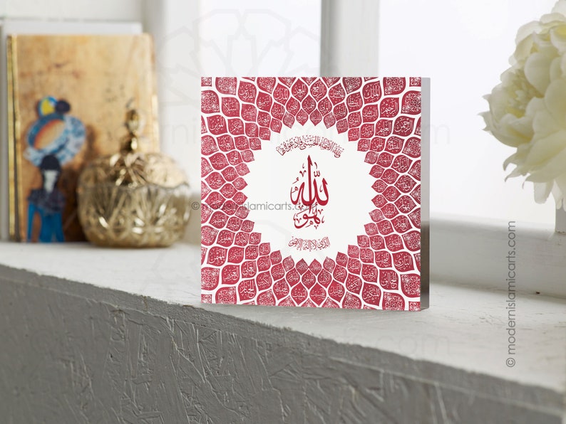 May include: A red and white square wall art piece with an intricate design of Arabic calligraphy. The design features a circular frame with the word "Allah" in the center, surrounded by a pattern of leaves.