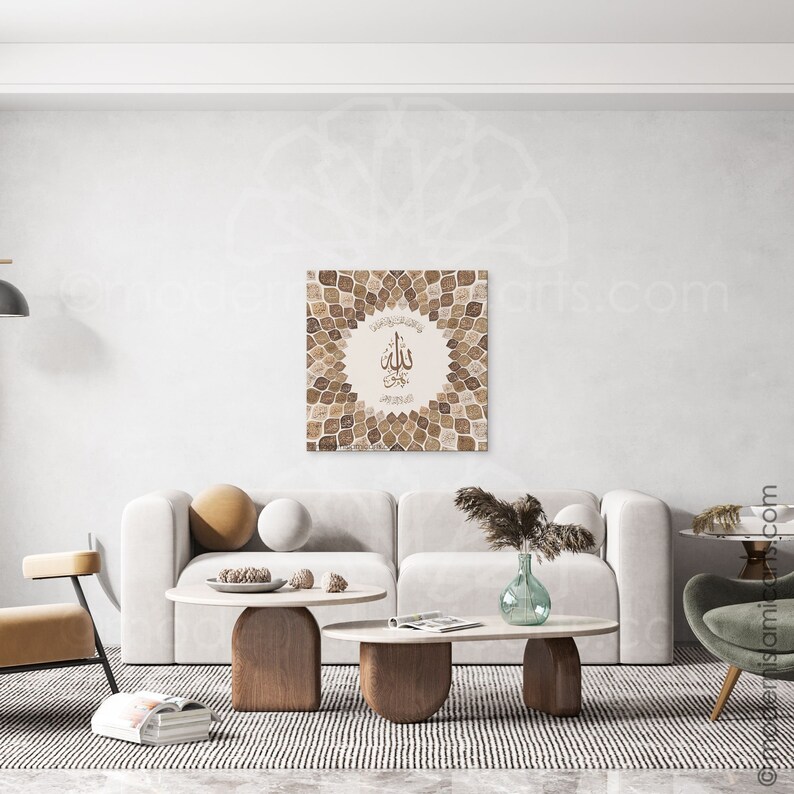 Puede incluir: Una impresi&oacute;n de arte de caligraf&iacute;a isl&aacute;mica beige y marr&oacute;n con la palabra "Allah" en el centro, rodeada de un patr&oacute;n geom&eacute;trico de hojas. La impresi&oacute;n est&aacute; colgada en una pared blanca sobre un sof&aacute; blanco con almohadas marrones y una mesa de caf&eacute; de madera.