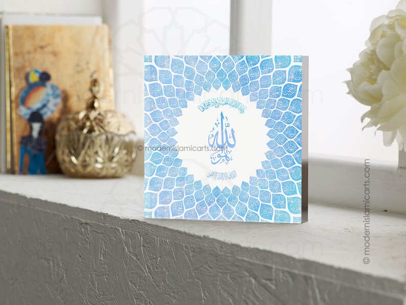 May include: A blue and white square wall decor with an intricate design of repeating leaf shapes. The center of the design features a white circle with Arabic calligraphy in black.