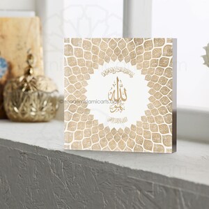 May include: A white square plaque with a gold geometric pattern and the Arabic word "Allah" in gold calligraphy. The plaque is surrounded by a border of gold leaves.