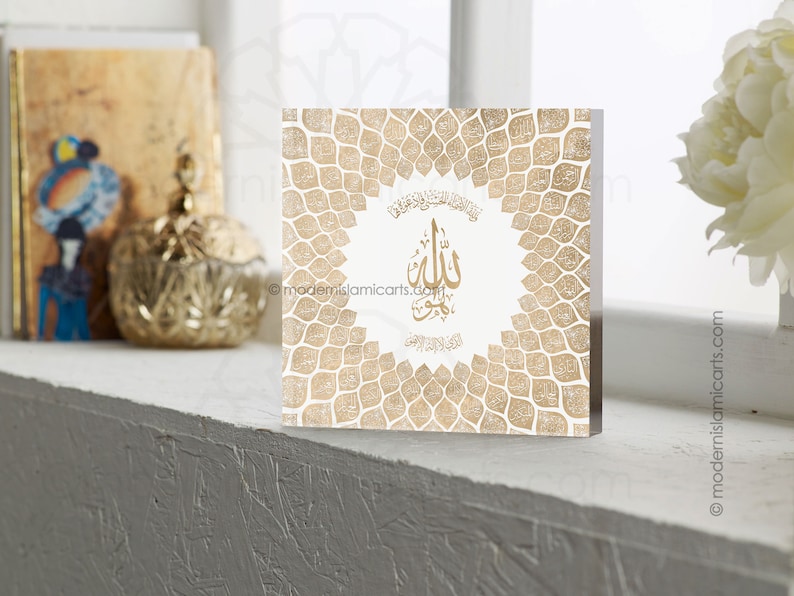 May include: A white square plaque with a gold geometric pattern and the Arabic word "Allah" in gold calligraphy. The plaque is surrounded by a border of gold leaves.