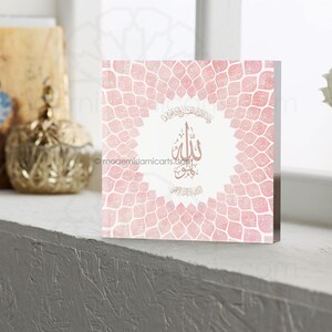 May include: A pink and white square wall art print with a gold Arabic calligraphy design that says "Allah" in the center. The background is a pattern of pink and white leaves.