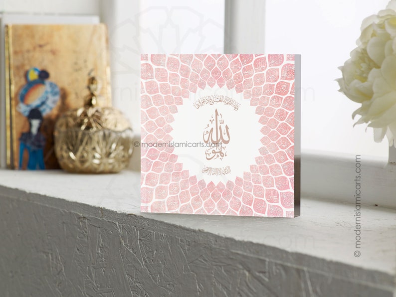 May include: A pink and white square wall art print with a gold Arabic calligraphy design that says "Allah" in the center. The background is a pattern of pink and white leaves.