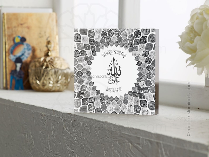 May include: A square, clear acrylic block with a black and white design. The design features a circular pattern of leaves with the word "Allah" written in Arabic calligraphy in the center.