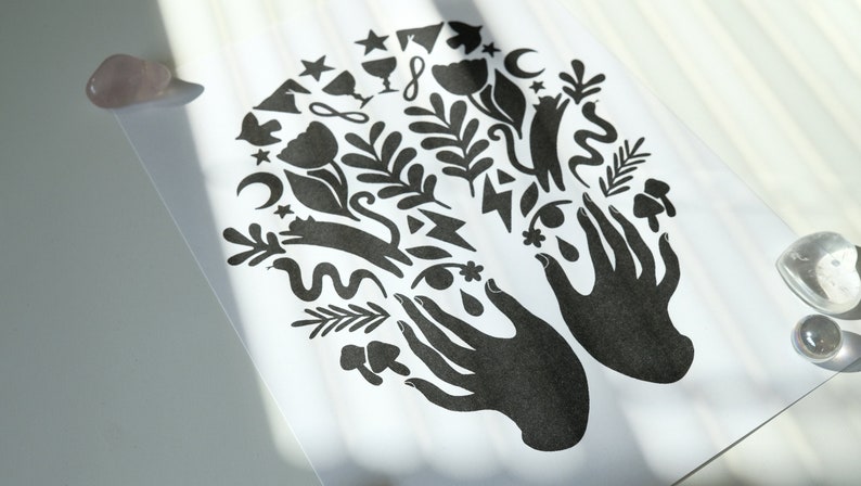 May include: Black and white print of two hands with various symbols and designs surrounding them, including stars, moons, flowers, and a cat.