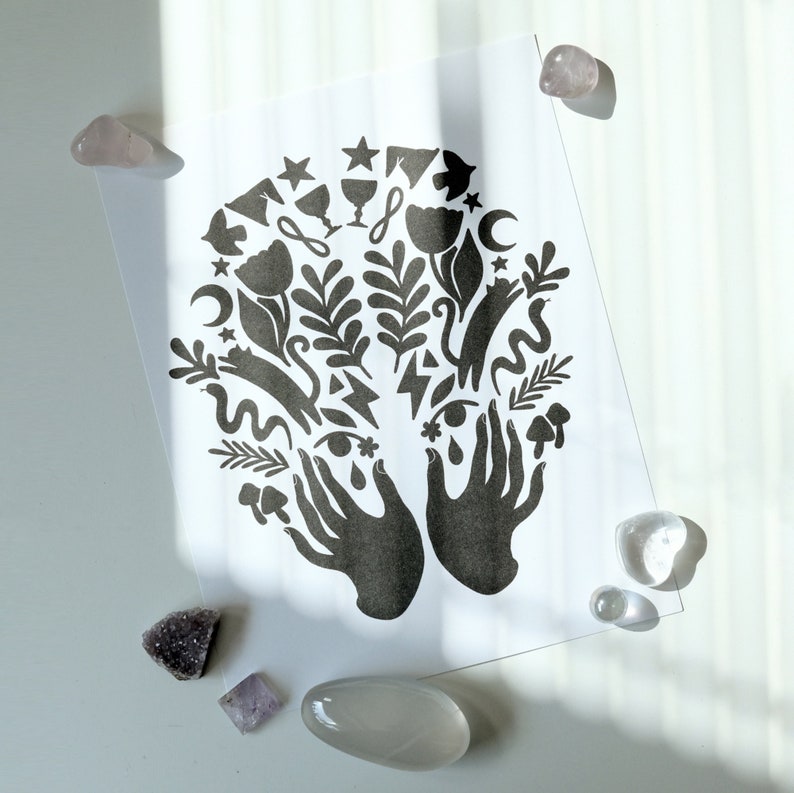 May include: Black and white print of two hands holding a variety of symbols, including stars, moons, flowers, and eyes. The print is on a white background.