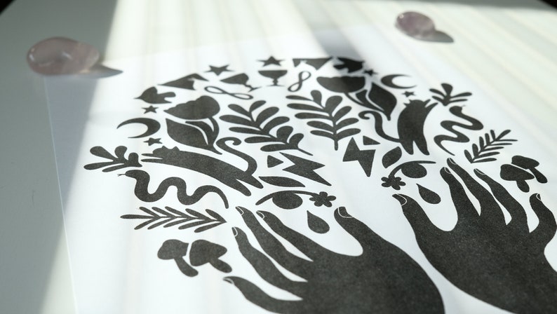 May include: Black and white print of two hands holding a variety of symbols, including flowers, stars, moons, snakes, and leaves.
