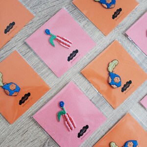 May include: A set of colorful embroidered iron-on patches featuring a vase with flowers. The patches are displayed on orange and pink cardstock with the word "mii" printed on each card.