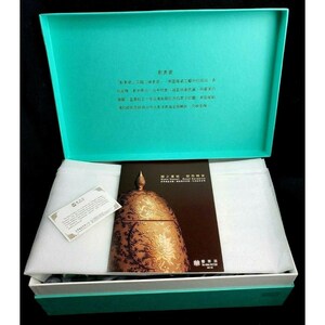 May include: An open turquoise gift box containing a decorative ceramic piece with a gold floral design. The box also holds a brochure and a small card. The ceramic piece has a domed lid and intricate patterns. The box is lined with white tissue paper.