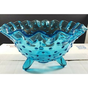 May include: A turquoise blue glass bowl with a ruffled rim and a dotted surface. The bowl has three legs and is perfect for serving snacks or desserts.