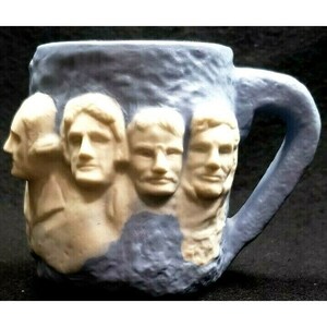 May include: A blue ceramic mug with a white image of Mount Rushmore. The mug features the faces of George Washington, Thomas Jefferson, Abraham Lincoln, and Theodore Roosevelt.