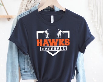 May include: Navy blue t-shirt with the text "HAWKS BASEBALL" in white and orange, featuring a baseball graphic. The shirt is hanging on a wooden hanger.
