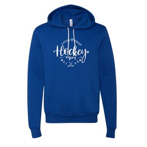 K&ouml;nnte beinhalten: Ein k&ouml;nigsblauer Hoodie mit Fronttasche und Kapuze mit Kordelzug. Der wei&szlig;e Text auf der Vorderseite lautet "Livin' that Hockey Mom Life" in Schreibschrift, mit Hockeyschl&auml;gern und Sternen.