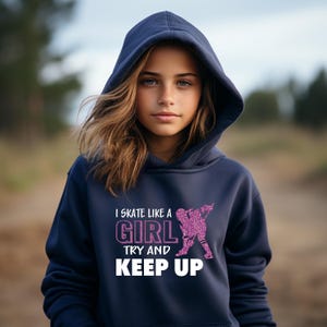 Puede incluir: Sudadera con capucha azul marino con el texto "I skate like a girl, try and keep up" en blanco y purpurina rosa. El gr&aacute;fico muestra una patinadora. La sudadera es de material suave.