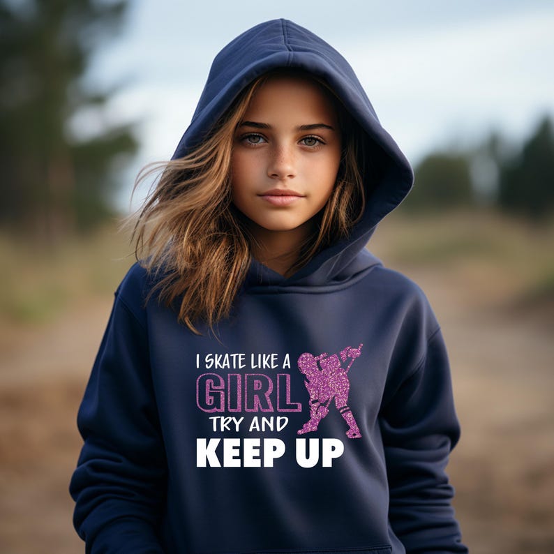 Puede incluir: Sudadera con capucha azul marino con el texto "I skate like a girl, try and keep up" en blanco y purpurina rosa. El gr&aacute;fico muestra una patinadora. La sudadera es de material suave.