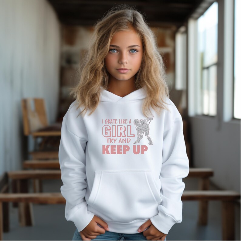 Puede incluir: Sudadera con capucha blanca con bolsillo delantero. El texto "I skate like a girl, try and keep up" est&aacute; impreso en rosa. Un gr&aacute;fico de un jugador de hockey est&aacute; al lado del texto. La sudadera es usada por una persona.
