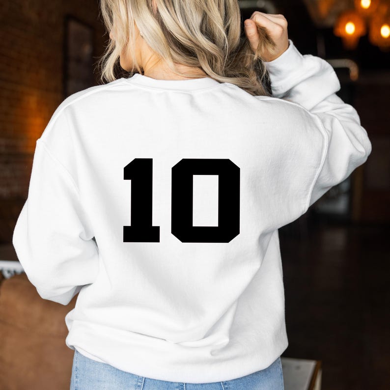 K&ouml;nnte beinhalten: Ein wei&szlig;es Sweatshirt mit der Nummer "10" in fetten, schwarzen Blockbuchstaben auf dem R&uuml;cken. Das Sweatshirt hat lange &Auml;rmel und einen Rundhalsausschnitt. Das Bild zeigt die R&uuml;ckseite des Kleidungsst&uuml;cks.