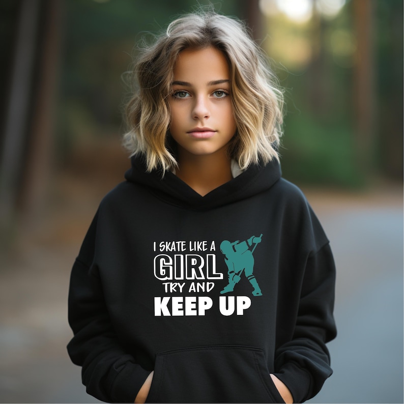 Puede incluir: Una sudadera con capucha negra con el texto "I Skate Like A Girl Try and Keep Up" en blanco y un gr&aacute;fico turquesa de un jugador de hockey. La sudadera con capucha la lleva una persona con cabello rubio.