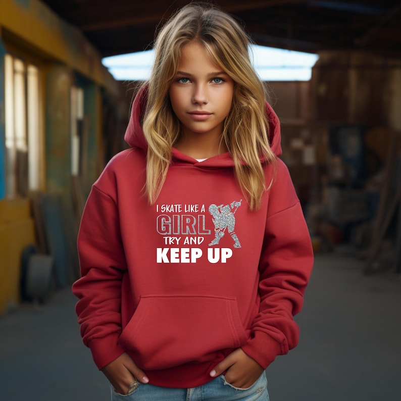 Puede incluir: Una sudadera con capucha roja con el texto "I skate like a girl try and keep up" en blanco y un gr&aacute;fico de patinadora con purpurina plateada. La sudadera tiene un bolsillo delantero y una capucha con cord&oacute;n.