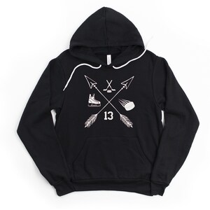 May include: Black hooded sweatshirt with a white graphic featuring crossed arrows, a hockey skate, a hockey stick and puck, and the number 13. The sweatshirt has a front pocket and white drawstring.