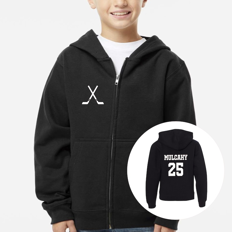 May include: A black zip-up hoodie featuring a white graphic of two crossed hockey sticks on the left chest. An inset circle shows the back of the hoodie, which displays the name MULCAHY in white block letters above the number 25 in white.