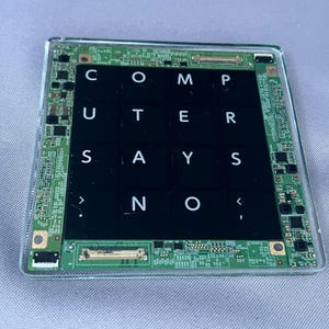 May include: A square coaster featuring a green circuit board border surrounding a black center grid. The grid contains white letters spelling out the phrase COMPUTER SAYS NO, with the text arranged in a four-by-four layout under a clear finish.
