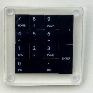 May include: A clear acrylic coaster with a black number pad printed on it. The numbers 0-9 are visible, along with the following keys: HOME, PGUP, PGDN, END, INS, DEL, ENTER, +, ←, ↑, →, ↓.