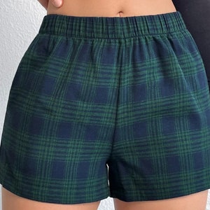 K&ouml;nnte beinhalten: Gr&uuml;n-marine karierte Shorts mit elastischem Bund. Die Shorts haben ein klassisches Karomuster in Gr&uuml;n- und Marineblaut&ouml;nen. Der Stoff scheint ein weiches, gewebtes Material zu sein.