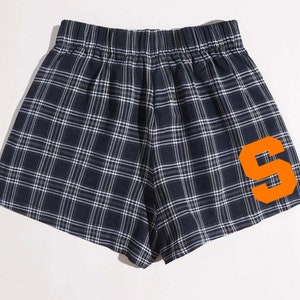K&ouml;nnte beinhalten: Marineblaue Shorts mit Karomuster und einem orangefarbenen Buchstaben "S" auf der Seite. Die Shorts haben einen elastischen Bund und ein klassisches Karo-Muster in Marineblau und Wei&szlig;. Bequeme und stilvolle Shorts.