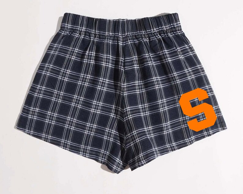 K&ouml;nnte beinhalten: Marineblaue Shorts mit Karomuster und einem orangefarbenen Buchstaben "S" auf der Seite. Die Shorts haben einen elastischen Bund und ein klassisches Karo-Muster in Marineblau und Wei&szlig;. Bequeme und stilvolle Shorts.