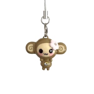May include: A brown monkey charm with a white flower and a silver chain. The charm has large black eyes, pink cheeks, and a small mouth. The monkey's belly has a clear gem. The charm is suspended from a silver chain.