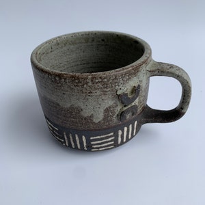 Könnte beinhalten: Eine braune und weiße Keramiktasse mit geometrischem Muster. Die Tasse hat eine gesprenkelte Glasur und einen Henkel.