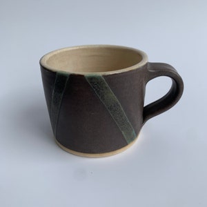May include: A brown ceramic mug with a white rim and green stripes. The mug has a rounded shape and a handle.