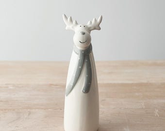 May include: A ceramic reindeer figurine with a white body, antlers, and a gray scarf with white polka dots. The reindeer has a smiling face and is a decorative item.