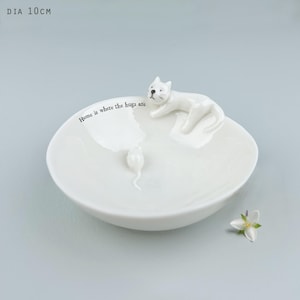 Może przedstawiać: Biały ceramiczny talerz o średnicy 10 cm, z motywem kota i myszy. Biały kot leży na brzegu, z figurką myszy w środku. Na talerzu znajduje się napis "Home is where the hugs are".