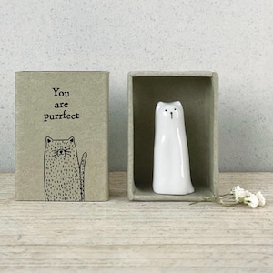 Könnte beinhalten: Eine weiße Keramik-Katzenfigur in einer grauen Schachtel, neben einer passenden Schachtel mit dem Text "You are purrfect" und einer Katzenillustration. Die Schachteln stehen auf einer Holzoberfläche.